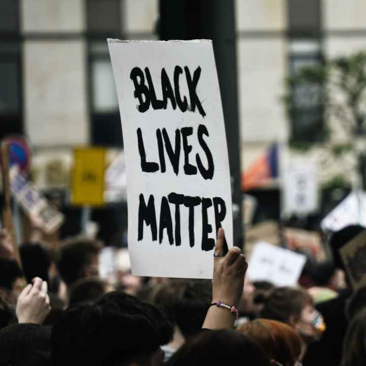 Black Lives Matter is handwritten in thick black on a white poster and held at a rally