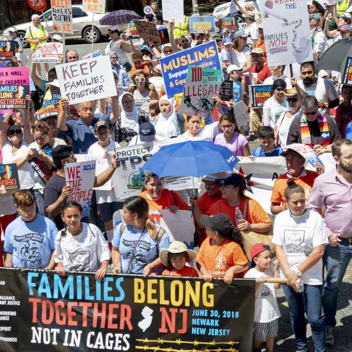 Group of protesters marching with banner reading "Families Belong Together. Not in Cages." 